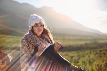 Young woman writing in journal in sunny, remote field - CAIF05086