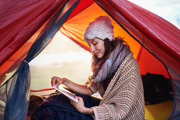 Junge Frau beim Zelten, mit digitalem Tablet im Zelt - CAIF05087