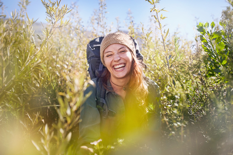 Porträt lachende junge Frau mit Rucksack Wandern in sonnigen Feld, lizenzfreies Stockfoto