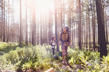 Young couple with backpacks hiking in sunny woods - CAIF05089