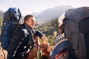 Junges Paar mit Rucksäcken beim Wandern, das eine Pause macht und Kaffee trinkt - CAIF05093