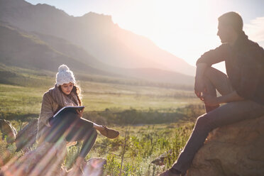 Young couple hiking, resting and writing in sunny remote field - CAIF05096