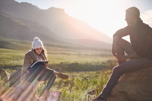 Junges Paar beim Wandern, Ausruhen und Schreiben in einem sonnigen, abgelegenen Feld - CAIF05096