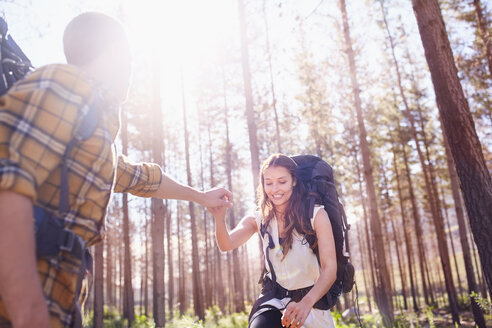 Junger Mann hilft Freundin mit Rucksack beim Wandern im sonnigen Wald - CAIF05102