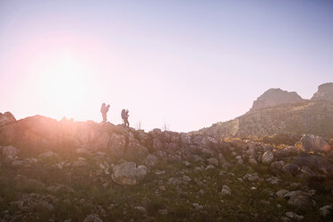 Young couple hiking along rock wall under sunny blue sky - CAIF05113