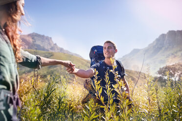 Junges Paar hält sich beim Wandern in einem sonnigen Tal an den Händen - CAIF05114