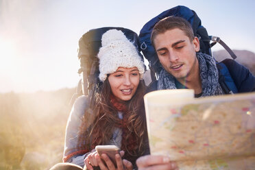 Young couple with backpacks hiking, checking map - CAIF05115