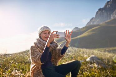 Junge Frau mit Fotohandy in einem sonnigen, abgelegenen Tal - CAIF05116
