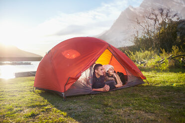 Junges Paar entspannt im Zelt auf einem sonnigen Campingplatz am See - CAIF05119