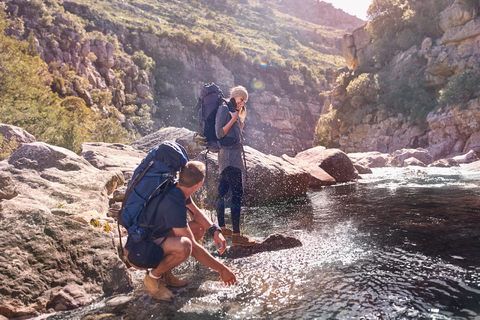 Junges Paar mit Rucksäcken beim Wandern, Wasser spritzen am Bach, lizenzfreies Stockfoto