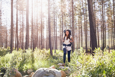 Lächelnde junge Frau mit Rucksack beim Wandern im sonnigen Wald - CAIF05131