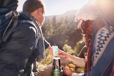 Junges Paar beim Wandern, das eine Kaffeepause macht und sein Smartphone benutzt - CAIF05134