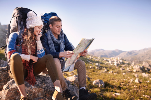 Junges Paar mit Rucksäcken wandernd, rastend und die Karte überprüfend auf sonnigen Felsen, lizenzfreies Stockfoto