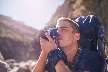 Junger Mann mit Rucksack beim Wandern und Fotografieren mit Kamera - CAIF05137