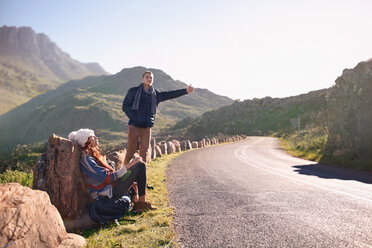 Young couple hitchhiking at sunny, remote roadside - CAIF05138