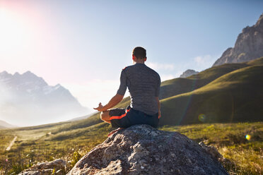 Young man meditating on rock in sunny, remote valley - CAIF05143