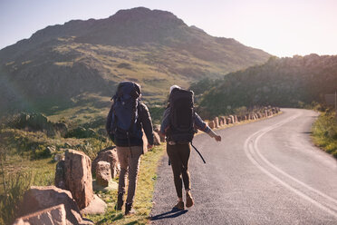 Young couple with backpacks hiking along sunny, remote roadside - CAIF05145