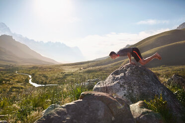 Young man balancing on hands on rock in sunny, remote valley - CAIF05146