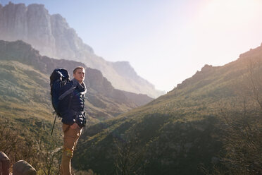 Junger Mann mit Rucksack beim Wandern, mit Blick auf die sonnige Bergwelt - CAIF05154