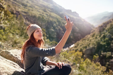 Junge Frau nimmt Selfie mit Kamera-Handy auf sonnigen, abgelegenen Felsen - CAIF05158