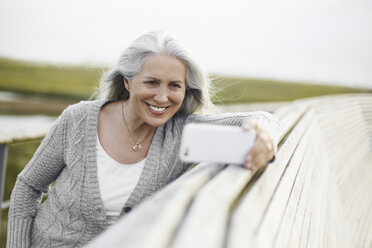 Lächelnde ältere Frau, die ein Selfie an der Strandpromenade macht - CAIF05174