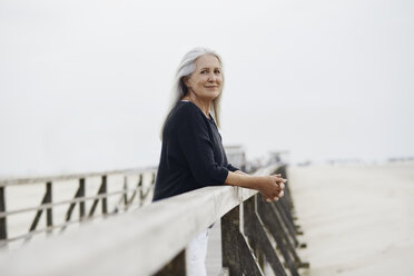 Porträt einer selbstbewussten älteren Frau, die sich auf das Geländer der Strandpromenade stützt - CAIF05175