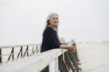 Portrait confident senior woman leaning on beach boardwalk railing - CAIF05175
