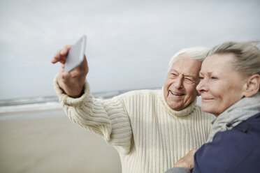 Älteres Paar macht Selfie mit Handy am windigen Winterstrand - CAIF05177