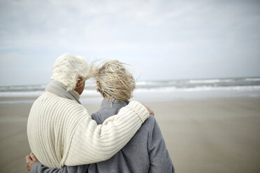 Nachdenkliches älteres Paar, das sich umarmt und auf das Meer blickt, an einem windigen Winterstrand - CAIF05179