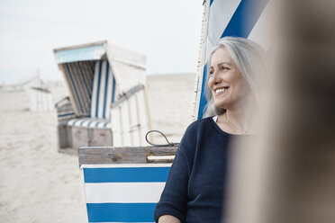 Lächelnde ältere Frau, die am Strand wegschaut - CAIF05180