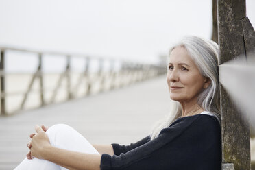 Pensive senior woman relaxing on beach boardwalk - CAIF05181