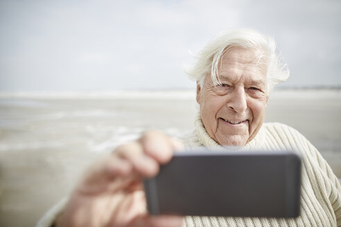 Lächelnder älterer Mann nimmt Selfie mit Handy am Strand - CAIF05183