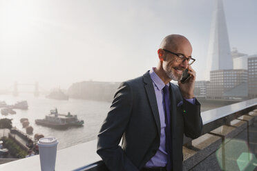 Geschäftsmann, der auf einer sonnigen, städtischen Brücke in London mit einem Handy telefoniert, Großbritannien - CAIF05187