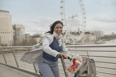 Porträt einer lächelnden Frau beim Fahrradfahren auf einer Brücke über die Themse in der Nähe des Millennium Wheel, London, UK - CAIF05189