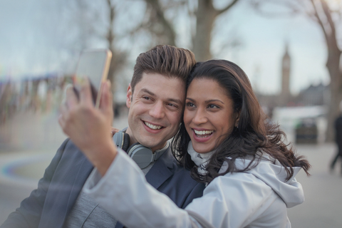 Lächelndes Paar macht Selfie mit Fotohandy im Stadtpark, lizenzfreies Stockfoto