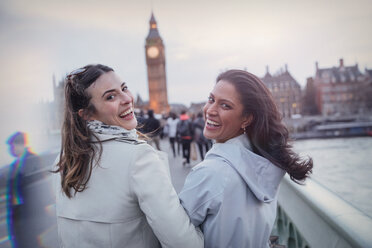 Porträt lächelnde, begeisterte Freundinnen, die auf einer Brücke in Richtung Big Ben gehen, London, UK - CAIF05193