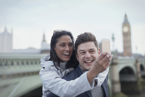 Playful, affectionate couple tourists taking selfie with camera phone in front of Westminster Bridge, London, UK stock photo