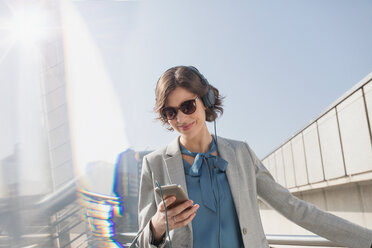 Smiling businesswoman with sunglasses listening to music with smart phone and headphones - CAIF05196