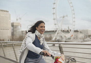 Begeisterte, lächelnde Frau beim Radfahren auf einer Brücke in der Nähe des Millennium Wheel, London, UK - CAIF05201