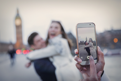 Persönliche Perspektive, verspieltes Paar, das sich umarmt und mit dem Fotohandy in der Nähe des Big Ben fotografiert wird, London, UK, lizenzfreies Stockfoto
