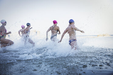 Female open water swimmers running and splashing in ocean surf - CAIF05208