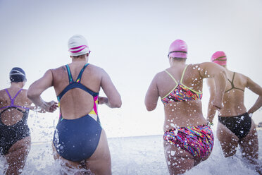 Female open water swimmers running and splashing in ocean surf - CAIF05211