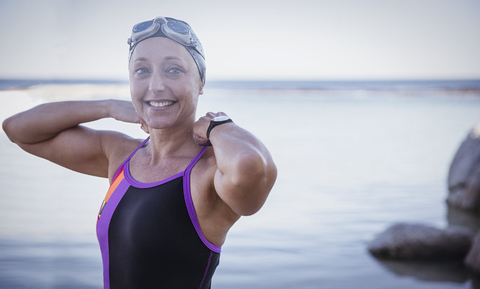 Porträt einer lächelnden Freiwasserschwimmerin, die ihren Badeanzug im Meer anpasst, lizenzfreies Stockfoto