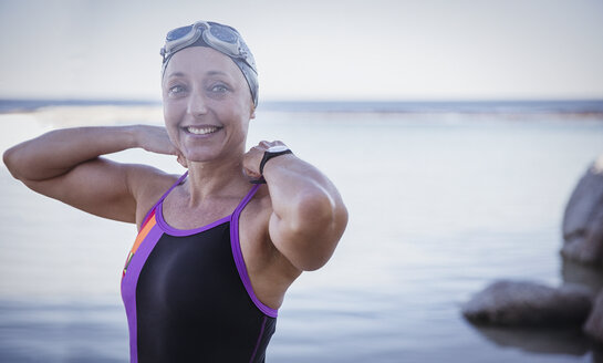 Portrait smiling female open water swimmer adjusting bathing suit in ocean - CAIF05216