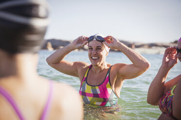 Lächelnde weibliche Freiwasserschwimmerinnen waten im sonnigen Meer - CAIF05220