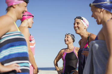 Lächelnde Freiwasserschwimmerinnen unterhalten sich am sonnigen Strand - CAIF05221