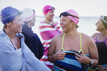 Weibliche Freiwasserschwimmer unterhalten sich und trocknen sich mit Handtüchern am Strand ab - CAIF05222