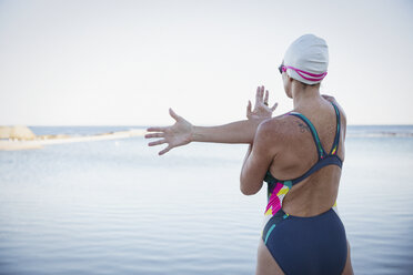 Female open water swimmer stretching arm and shoulder at ocean - CAIF05233