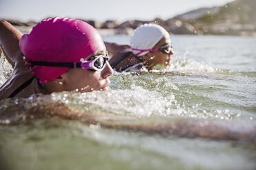 Female open water swimmers swimming in sunny ocean - CAIF05234