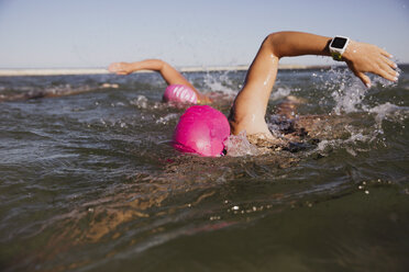 Freiwasserschwimmerin mit Smartwatch schwimmt im sonnigen Meer - CAIF05239